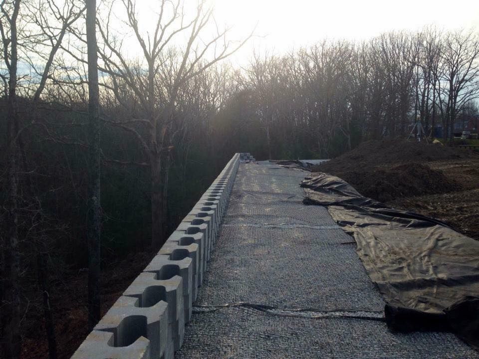 Concrete block wall, gravel pathway, trees. Partially constructed road through a wooded area.