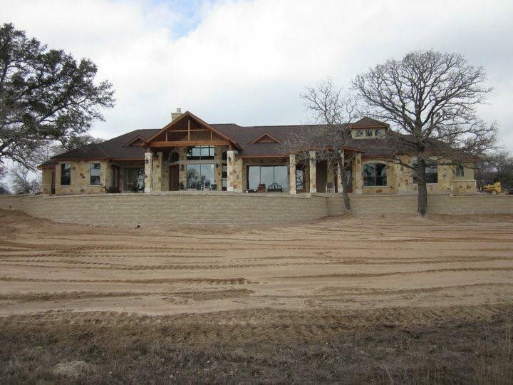 Large stone house on a raised foundation with a brown roof and windows, set in a field.