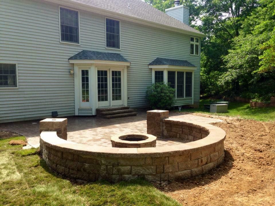 Backyard patio with curved brick fire pit and house in background.