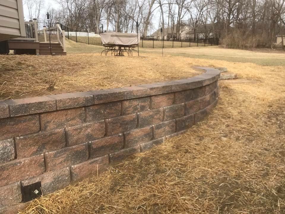Curved retaining wall made of reddish-brown bricks in a yard with dry grass; outdoor setting.