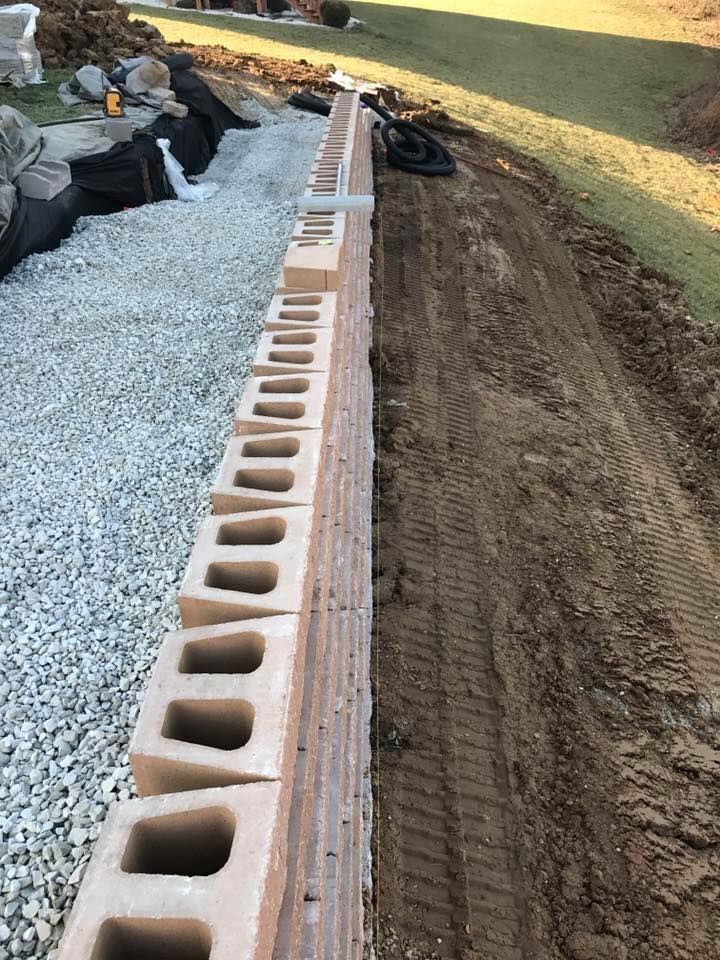 Retaining wall under construction, made of stacked concrete blocks, gravel bed on one side, dirt on the other.