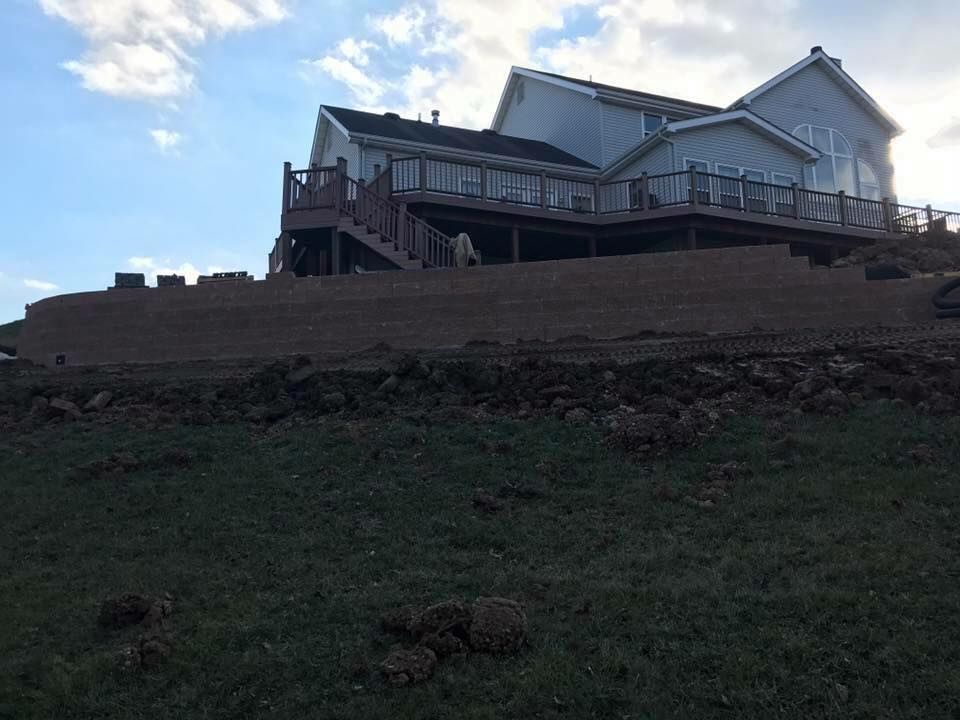 House with large deck on a hillside, recently graded dirt in the foreground, blue sky.