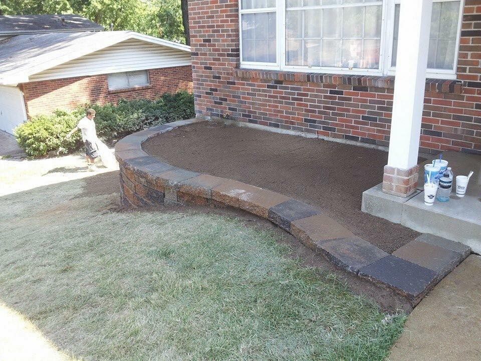 Front porch with low stone wall. Gravel-filled area, brick house, and green grass.