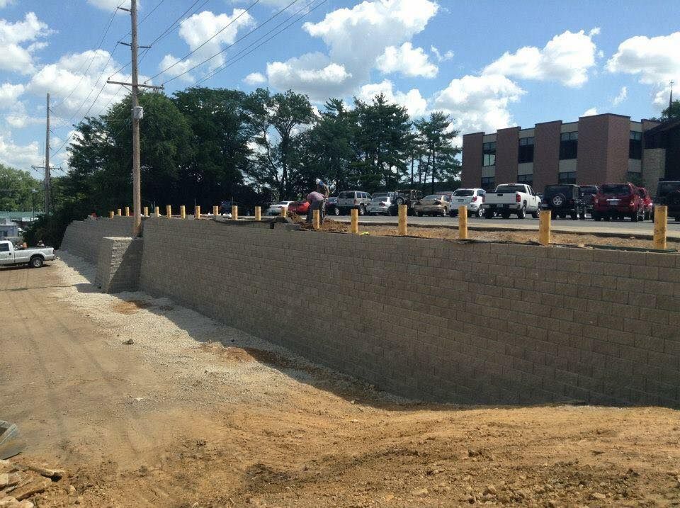 A tall retaining wall constructed of stone with a parking lot and building in the background.