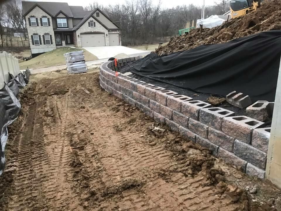 Retaining wall under construction near a house, with dirt and construction materials present.