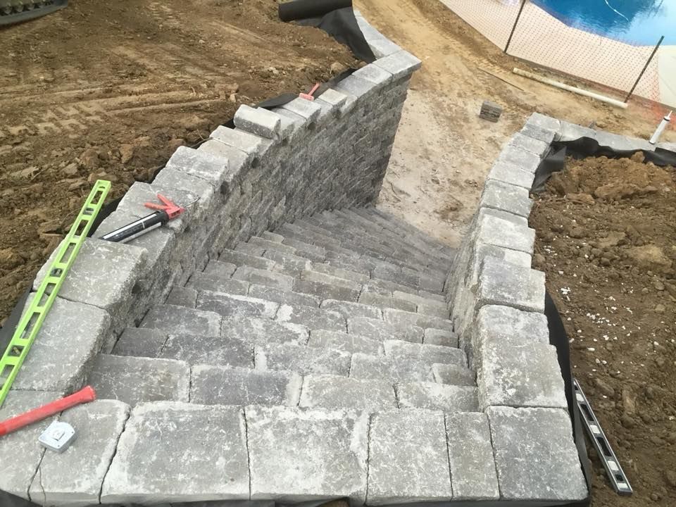 Stone staircase under construction near a pool. Gray blocks form the steps and retaining walls.