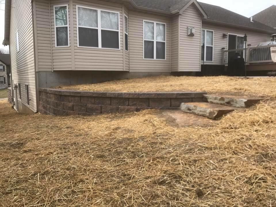 Backyard with retaining wall, steps, and house in the background, on dry grass.