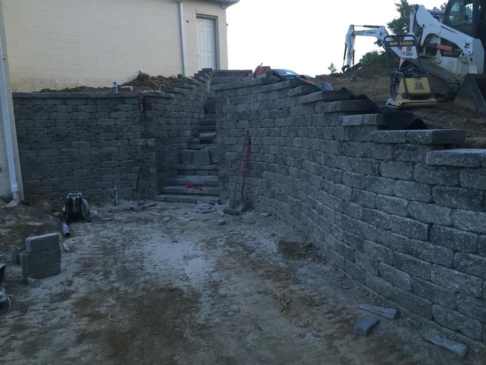 Construction site with stone retaining walls and stairs leading up a hillside.