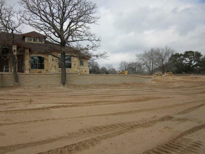 House and bare trees on a dirt lot, tire tracks in foreground, overcast sky.