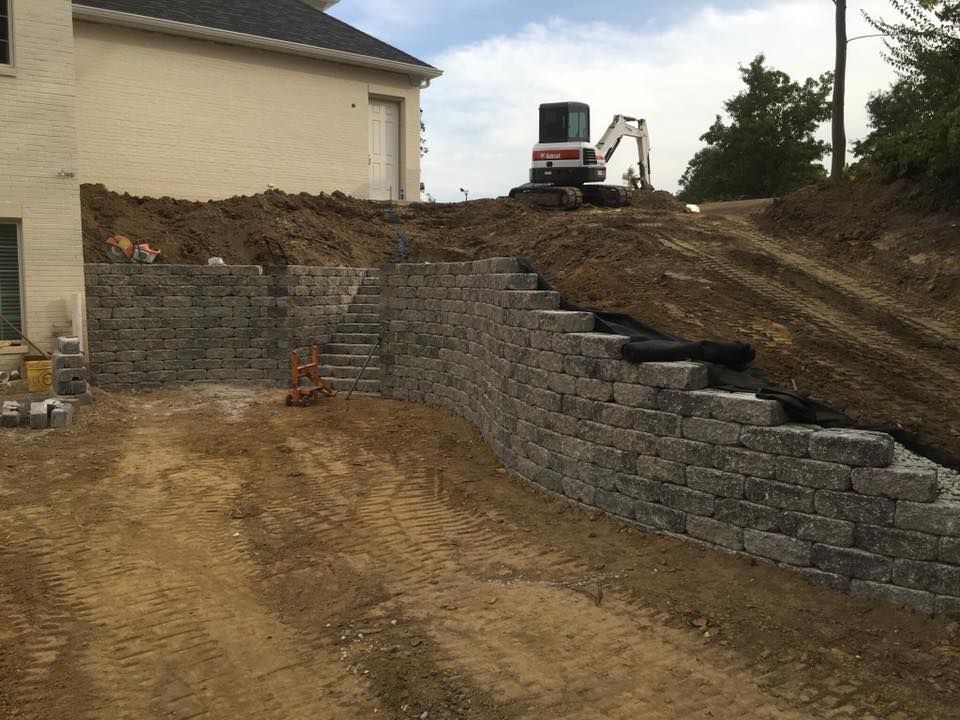 A hillside retaining wall made of grey stone blocks under construction with an excavator.