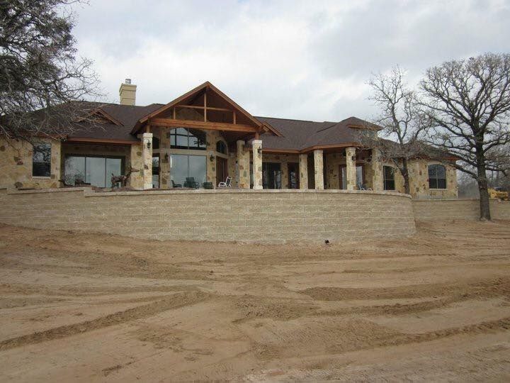 Large house with stone facade, a raised patio, and brown roof on a cloudy day.