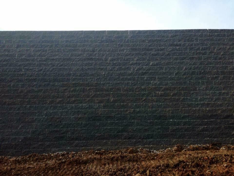 A dark, textured retaining wall against a light sky, built from stacked blocks.