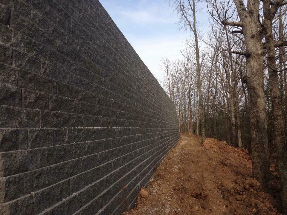 Dark gray retaining wall alongside a dirt path, trees in background.