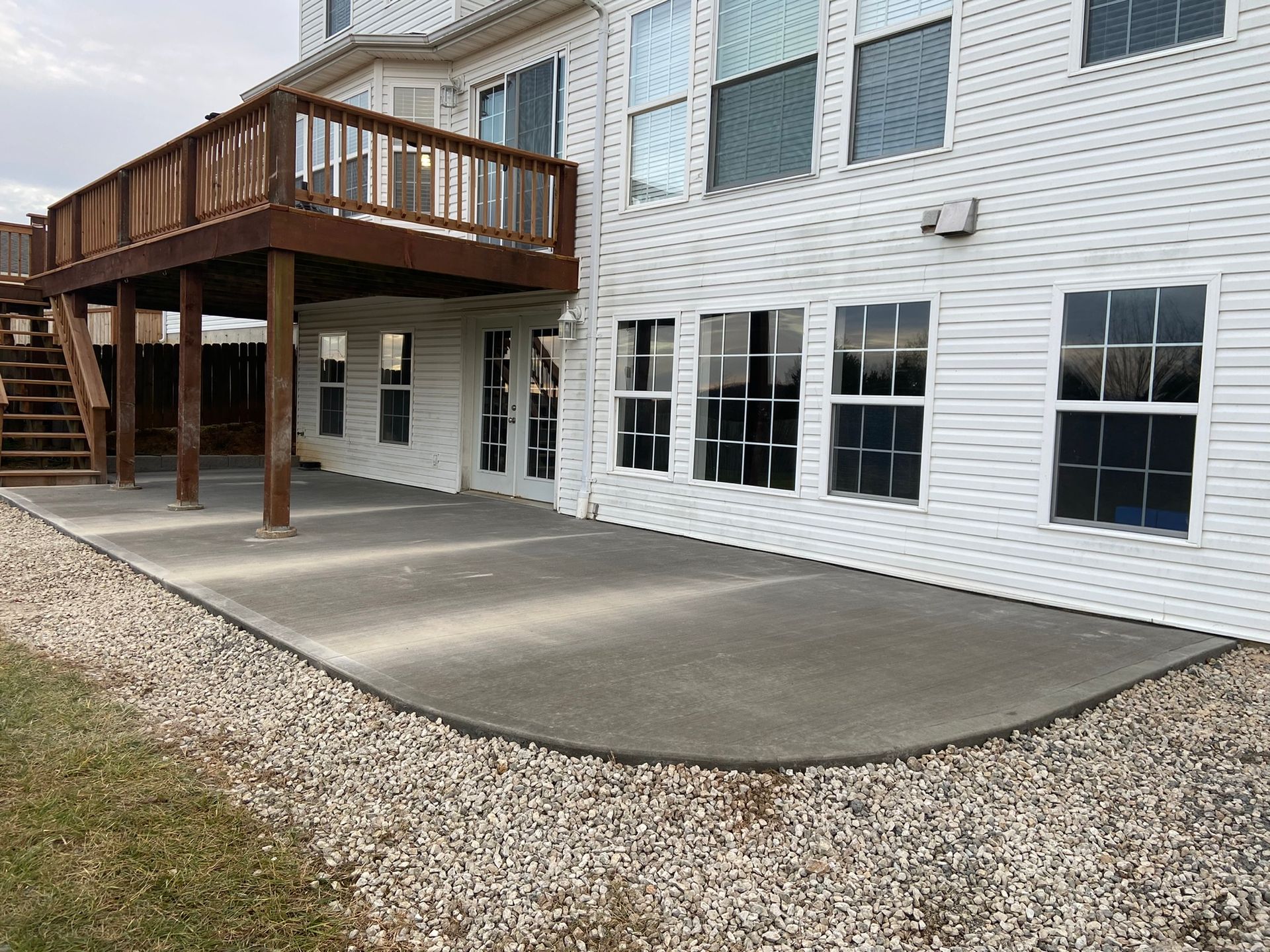 Concrete patio next to a white house with a wooden deck. The patio is bordered by gravel.
