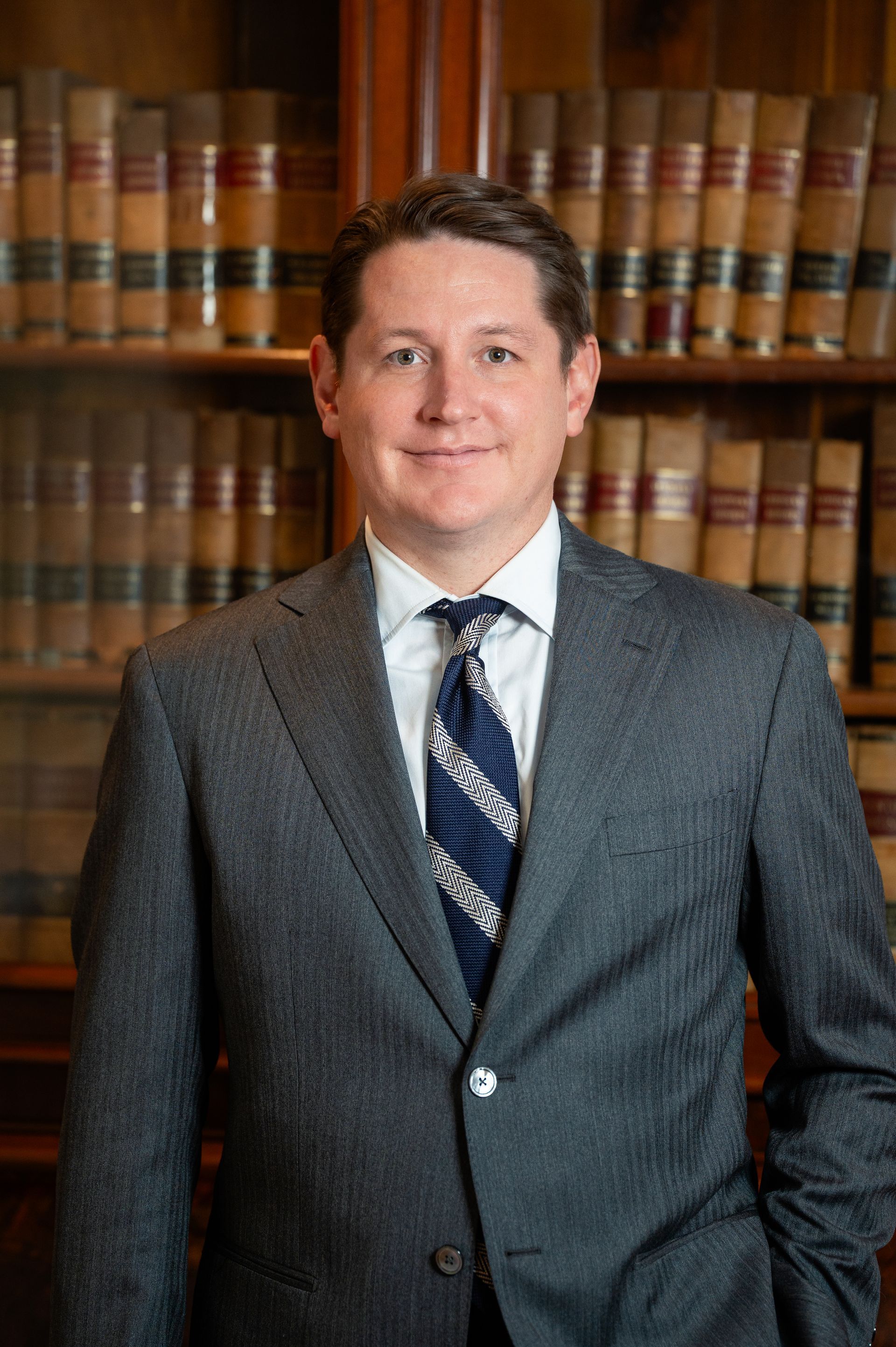 Man in suit smiles in front of a bookcase filled with law books.