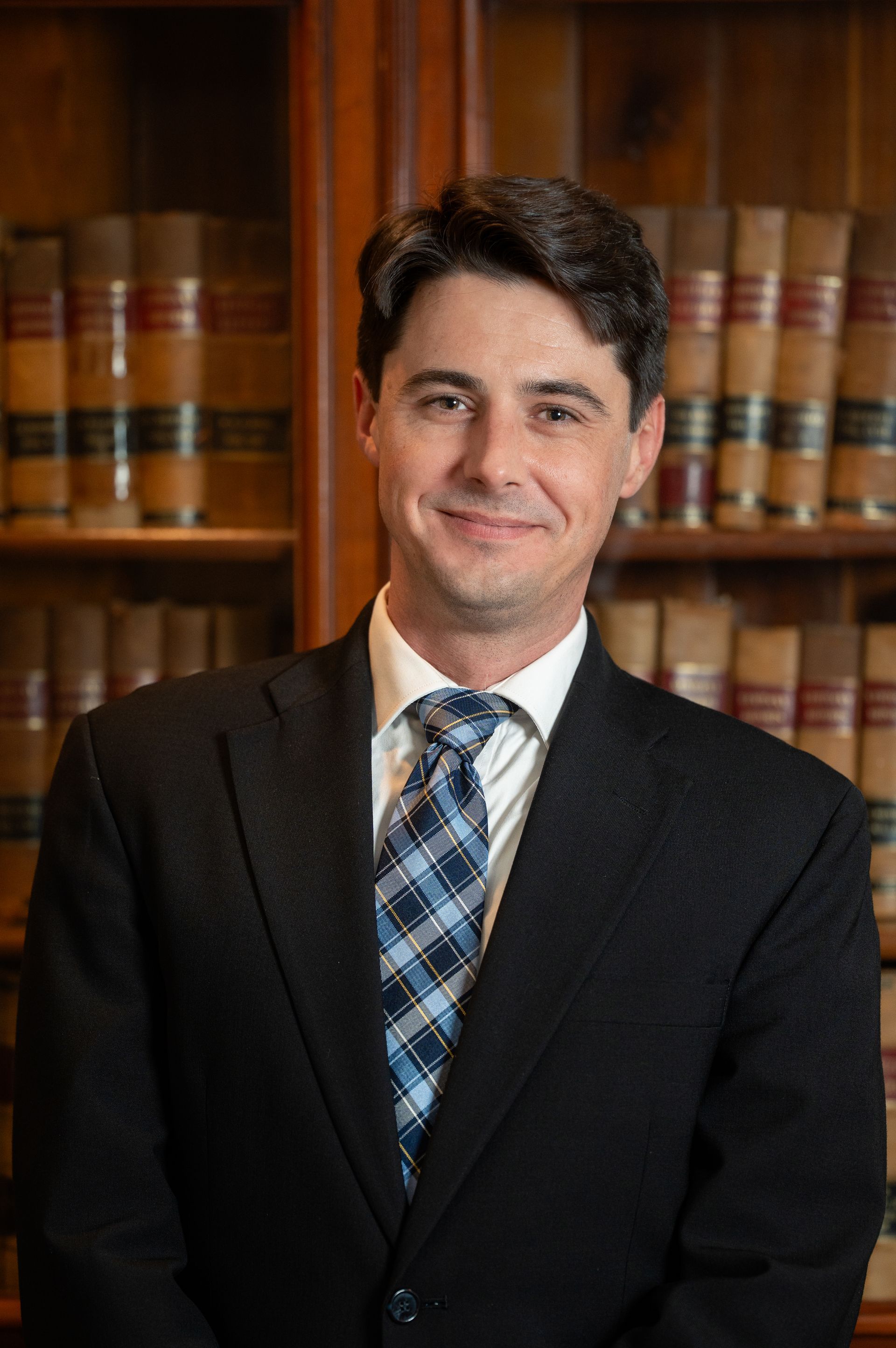 Man in suit and tie smiles in front of a bookshelf.