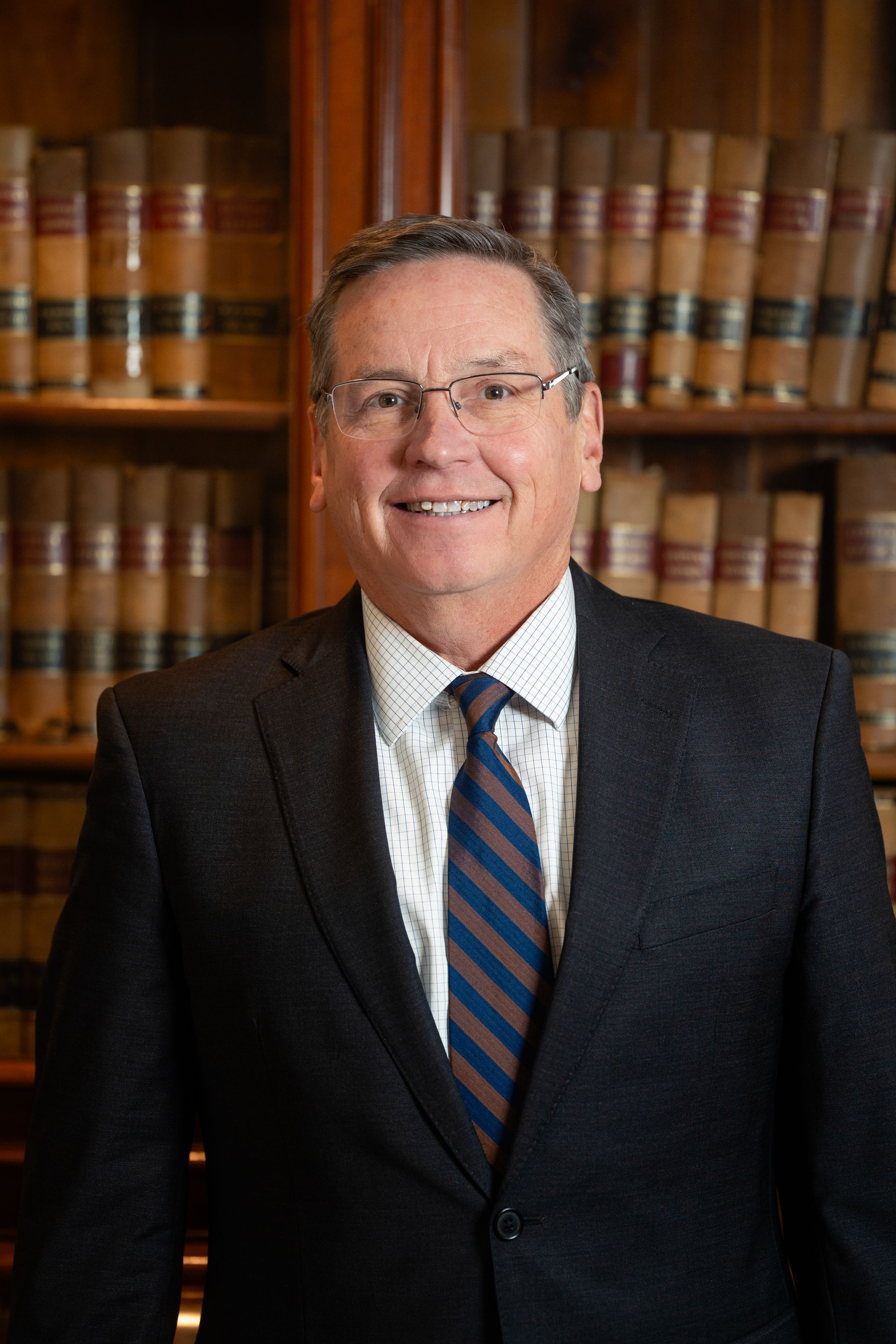 Man in a suit smiles in front of a bookcase filled with books.