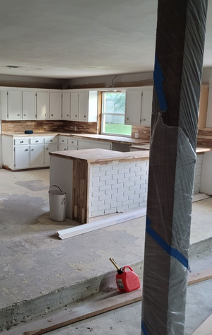 Unfinished kitchen with white cabinets, central island, exposed columns, and construction tools on the floor.