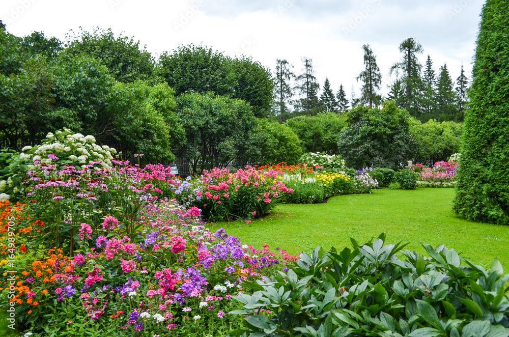 Two workers in high-visibility vests install a white drainage pipe in a backyard trench near a house and flower beds.