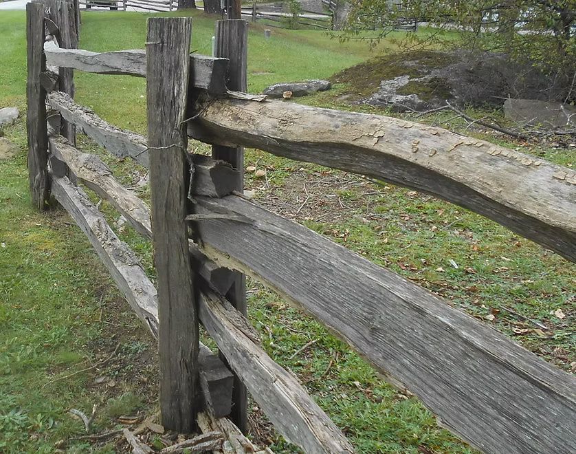 A rustic wooden split-rail fence stretches across a green, grassy field.