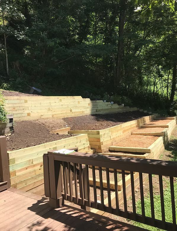 A view from a wooden deck showing a newly constructed tiered garden bed made of light-colored timber beams.