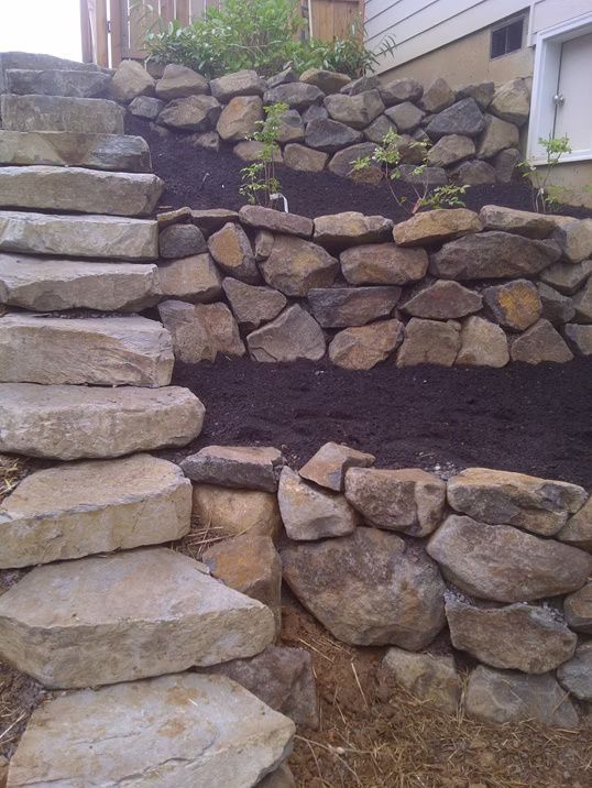 Stone steps lead up alongside a tiered garden featuring rock retaining walls and dark mulch.