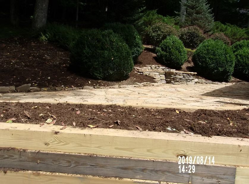 Freshly installed wooden retaining walls framing a stone patio and garden beds with rounded shrubs.