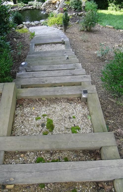 Outdoor wooden steps leading down to a pond, featuring gravel-filled treads and embedded solar lights.