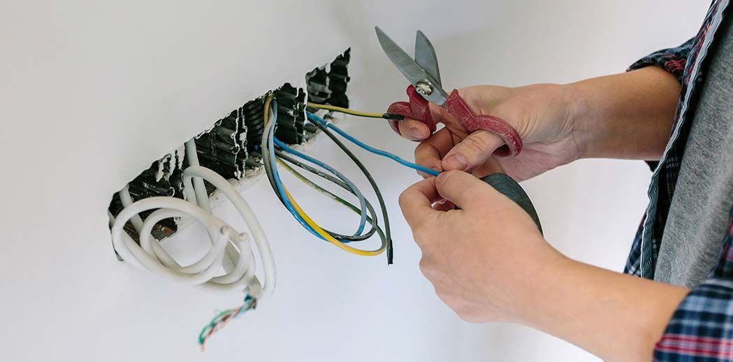 A Person Uses Scissors to Cut a Electrical Wire — Premiair Refrigeration, Air Conditioning & Electrical in Tamworth, NSW