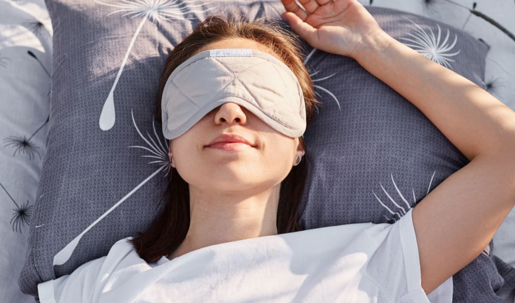 Woman wearing a sleep mask, lying on a pillow, eyes closed.