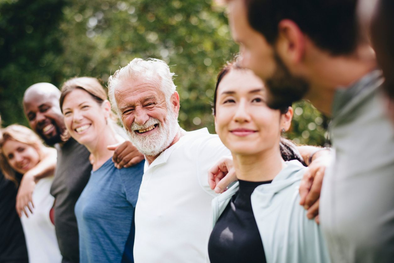 Group of people smiling, arms around each other in an outdoor setting.