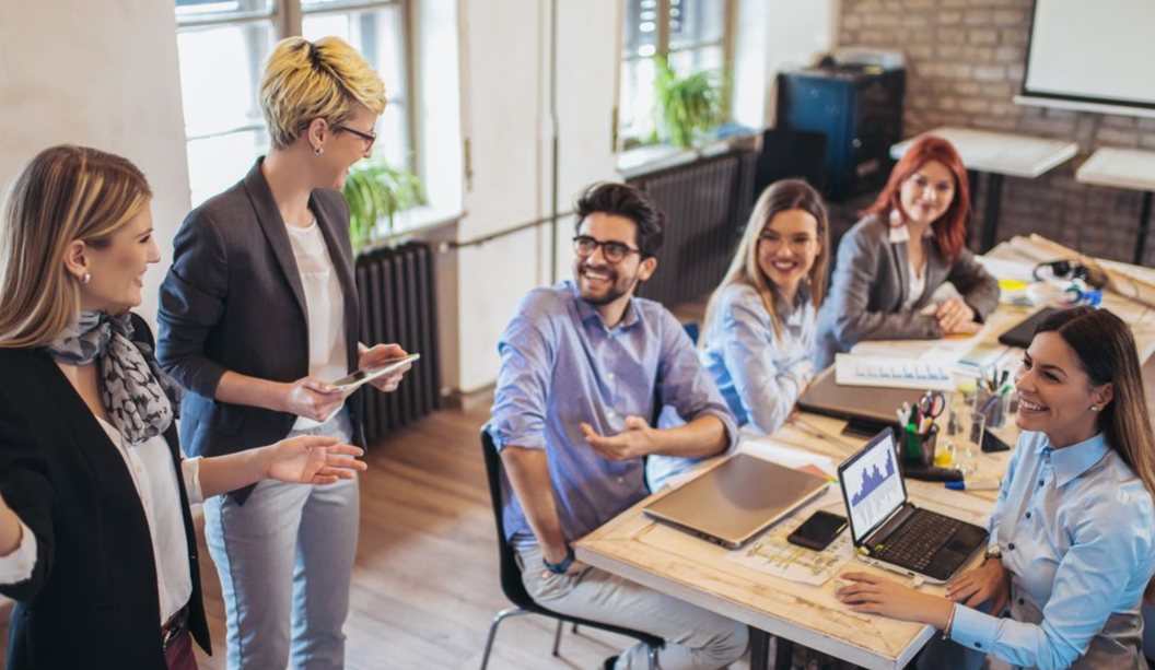 Team in a meeting, smiling and talking around a table in a modern office.