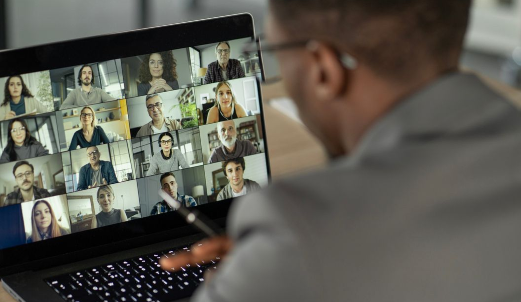 Person in suit, attending a video conference on a laptop with many participants.