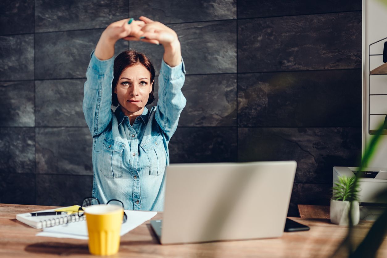 Woman at desk with head in hands, stressed, laptop, notebook, phone.