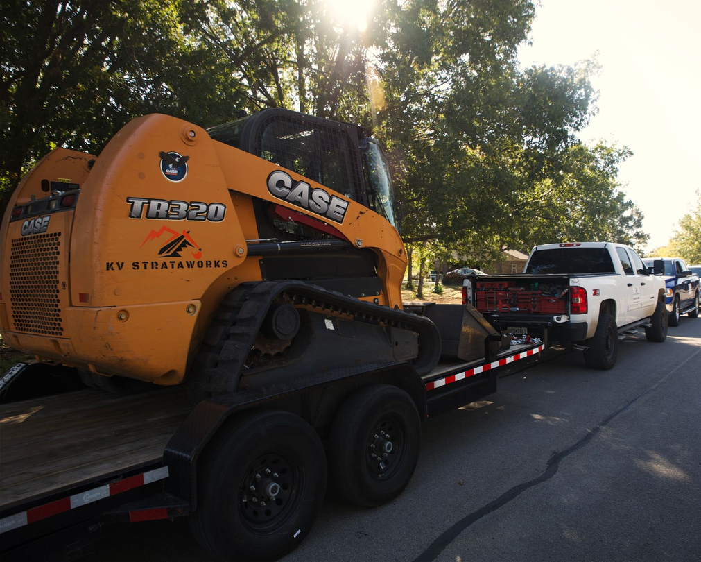 A white Bobcat track loader with a full bucket of dirt on a worksite in bright sunlight.