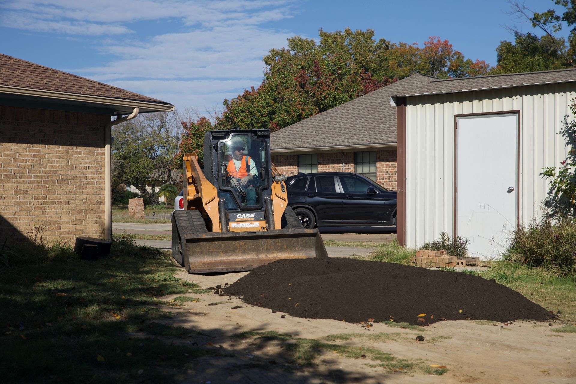 Skid steer performing grading work, smoothing and leveling soil for a new construction area.