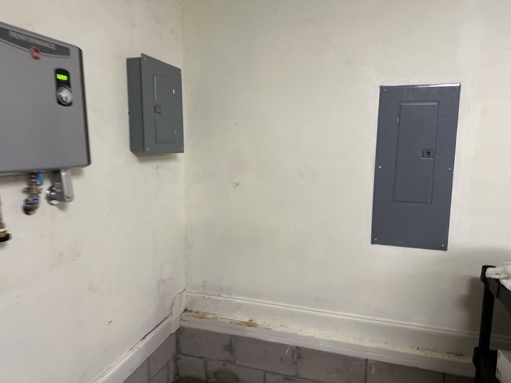 Electric water heater installation near electrical panels in residential Wilmington, NC home