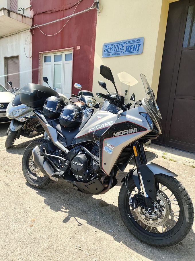 Due motociclette da avventura parcheggiate davanti a un edificio con un'insegna blu e la porta aperta.