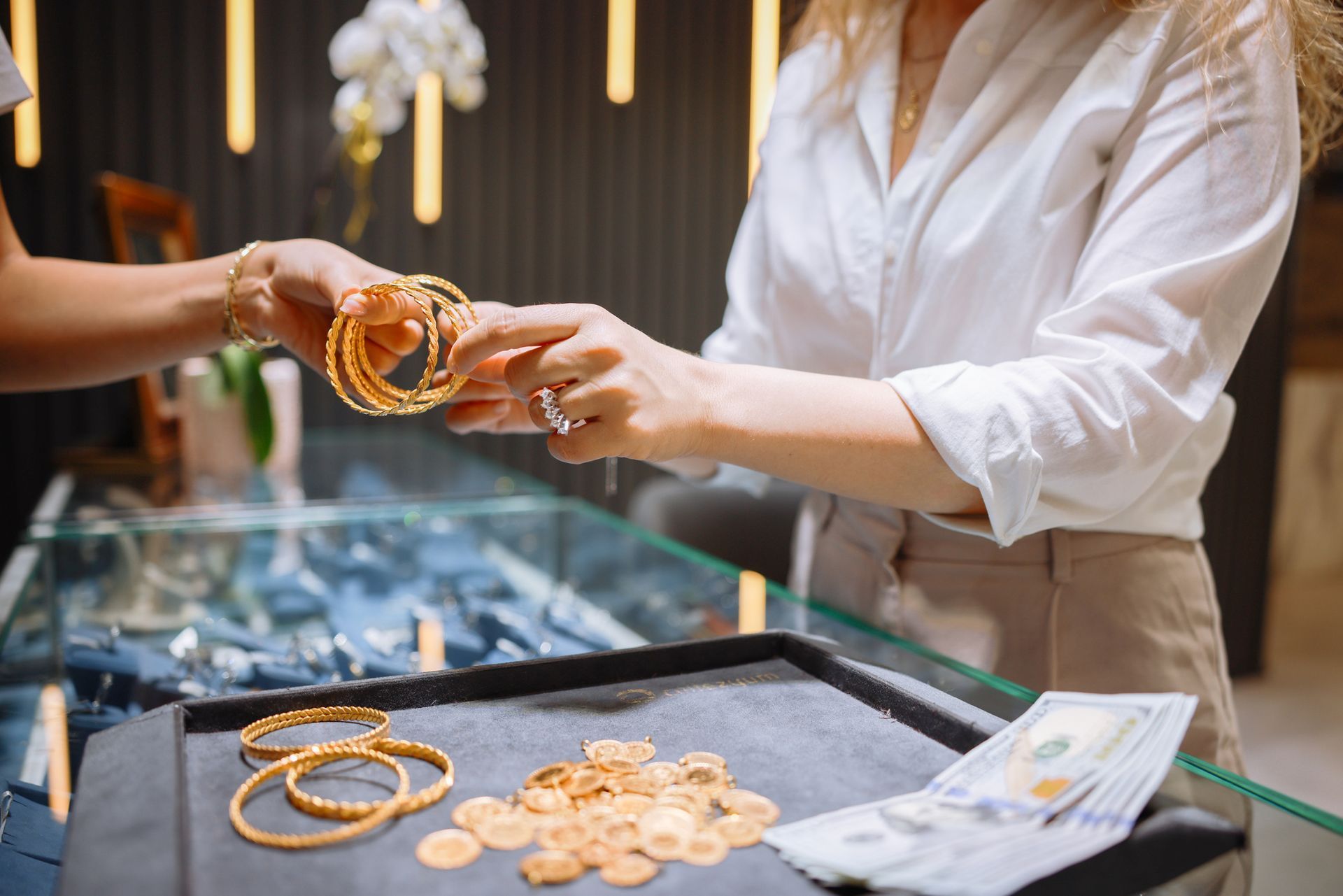 Close-up of a woman selling gold bracelets to gold buyers at a jewelry store counter.
