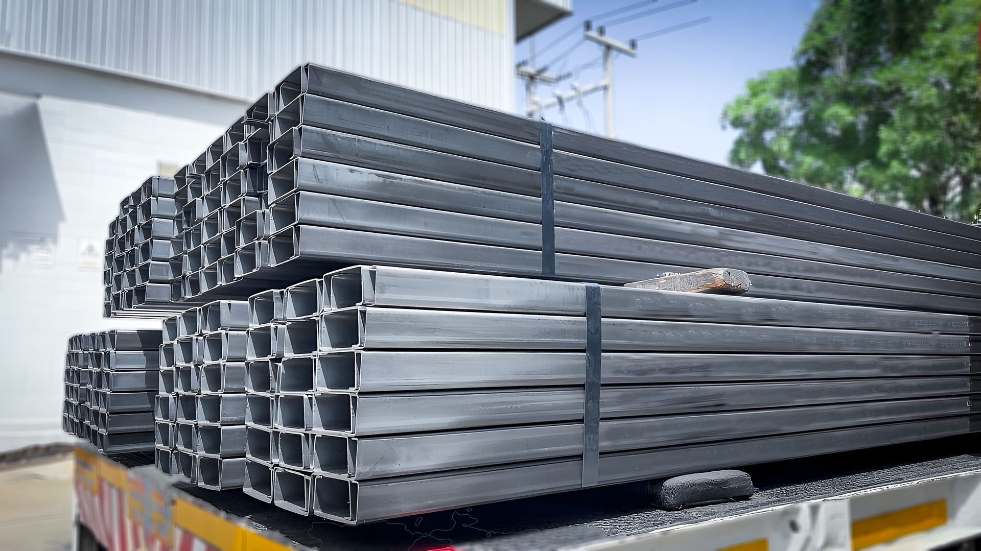 Large bunches of steel H-beams on top of a truck bed parked outdoors.