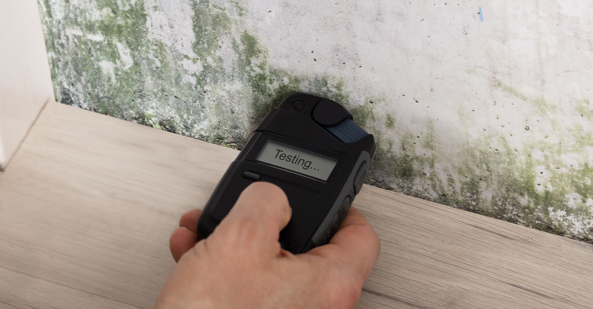 A person is using a mould detector on a wall.