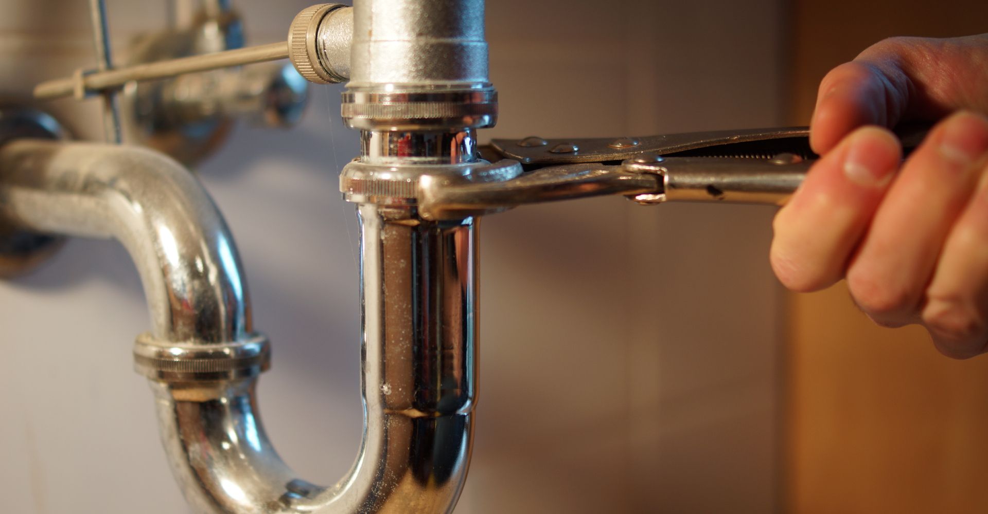 A person is fixing a sink pipe with a wrench.