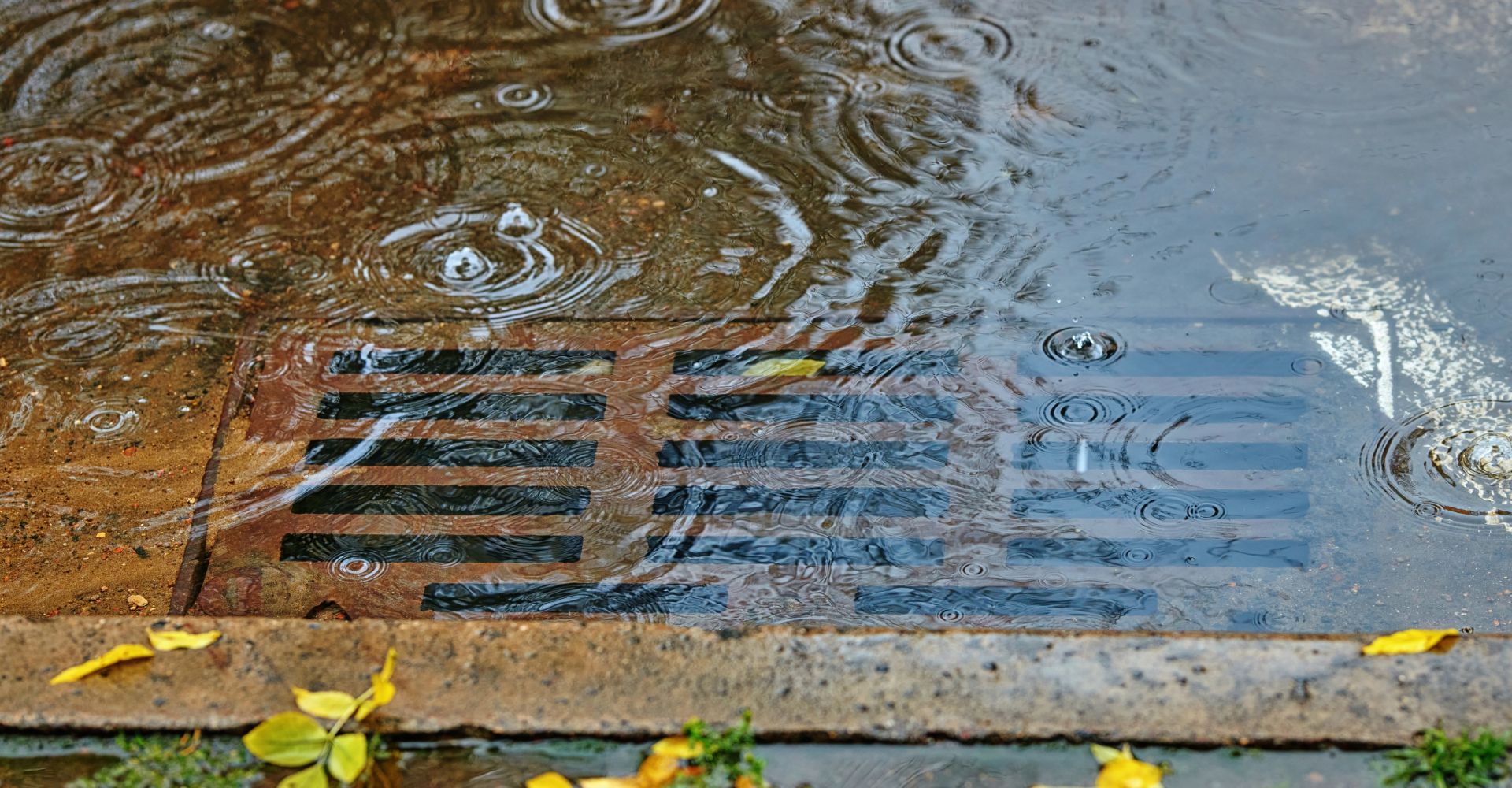 A drain with water coming out of it on a rainy day.