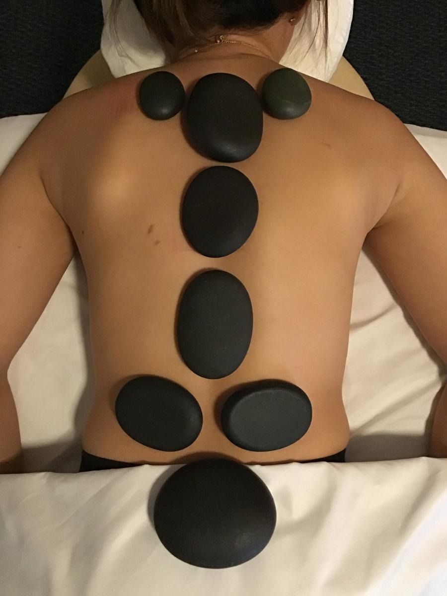 Person lying face down, with hot stones placed along their back in a spa setting.