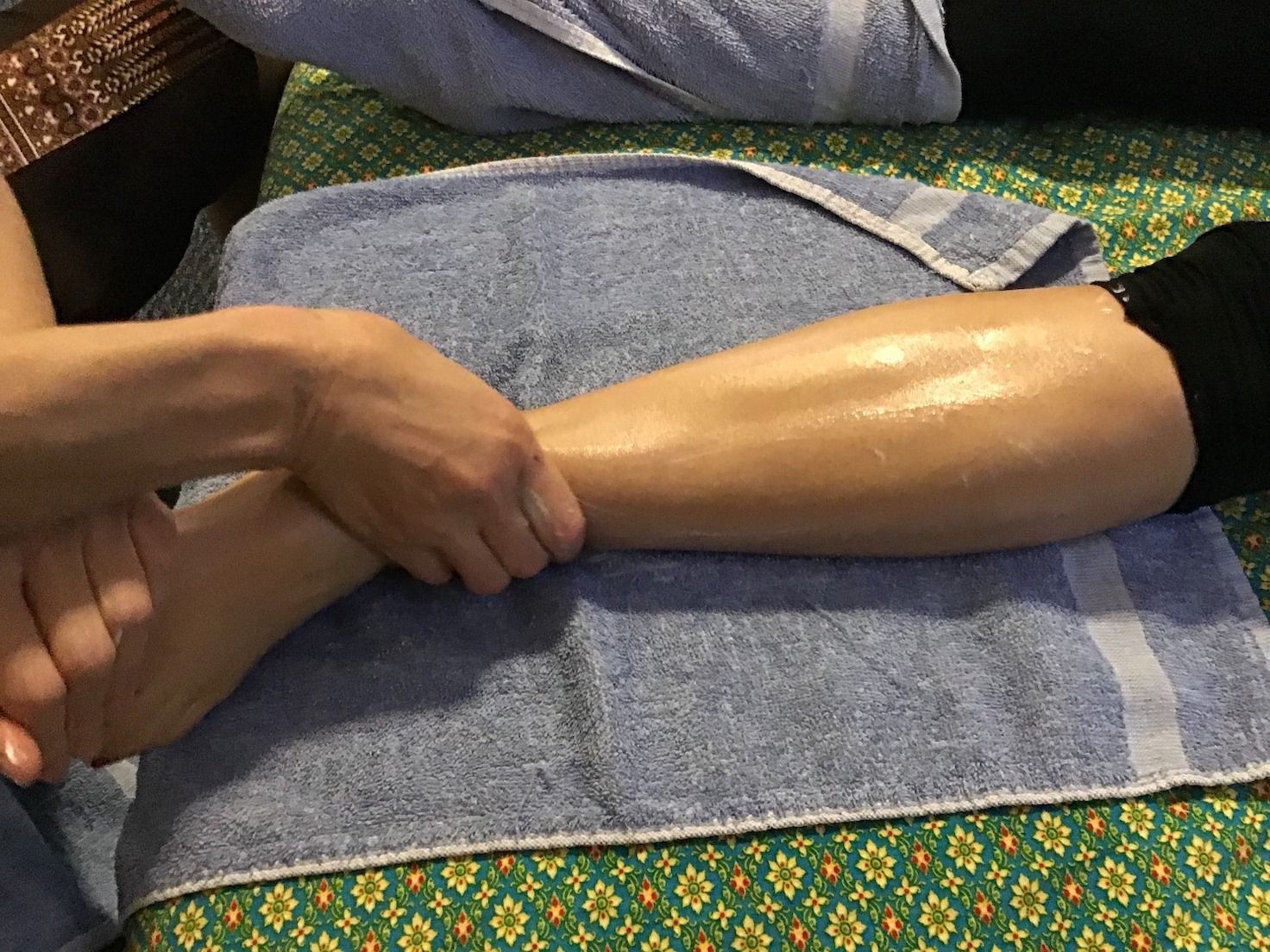 Hands massaging a leg on a blue towel, likely for a therapeutic massage.