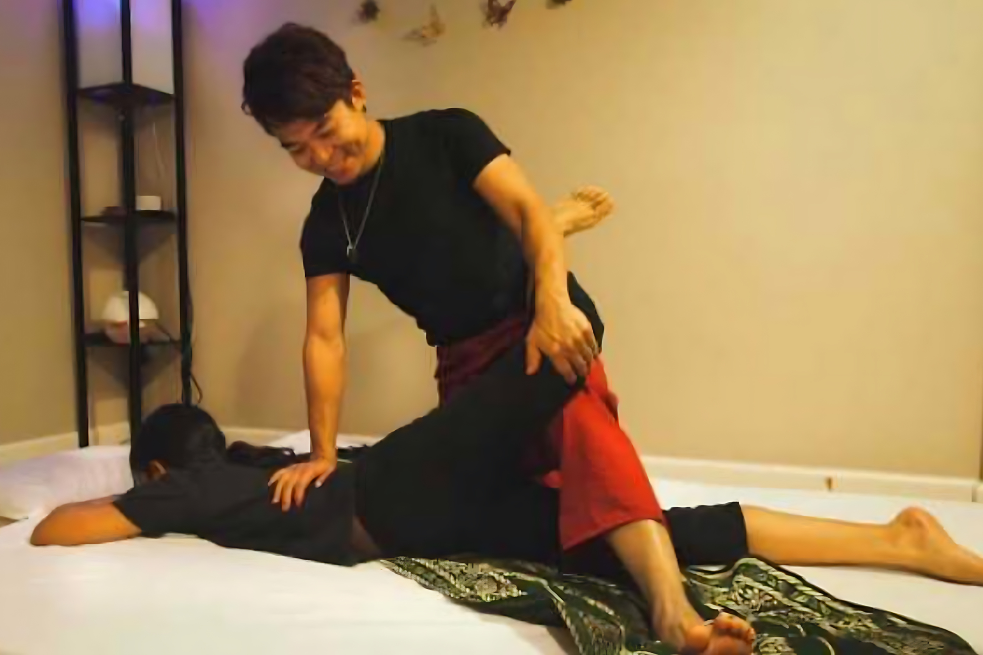 Man giving massage to person lying face down on a bed.