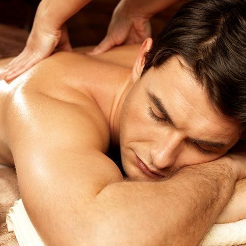 Man receiving a back massage; lying face down, eyes closed, being massaged on his back.