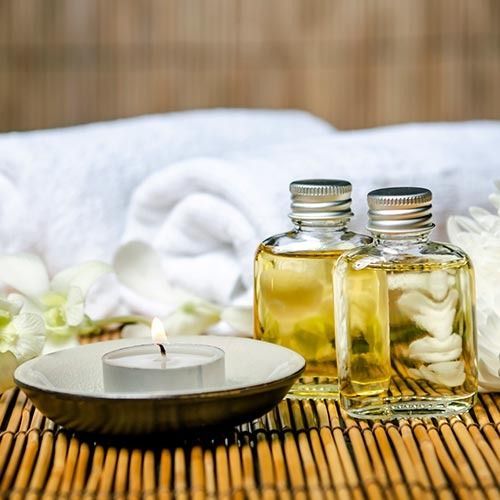 Spa scene: two bottles of oil, candle, rolled white towel, and flowers on bamboo mat.