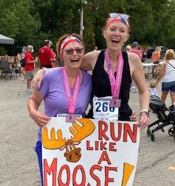 Two women holding a sign that says run like a moose