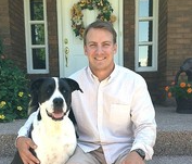 A man is sitting on the steps of a house with a black and white dog.